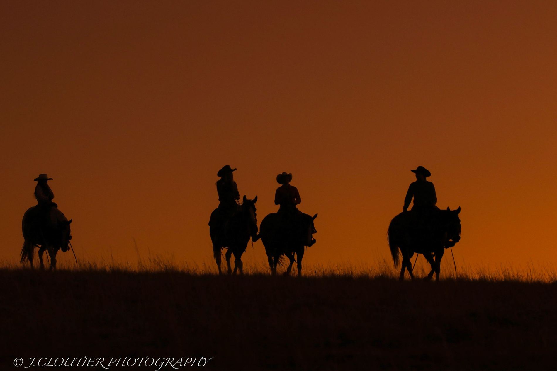 Riders on horseback silhouetted against a glowing Western sunset
